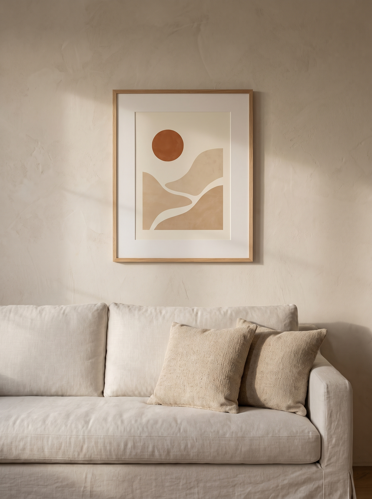 Stampa incorniciata Sole Astratto, disco solare terra di Siena su curve color sabbia, cornice in rovere, appesa sopra un divano in lino